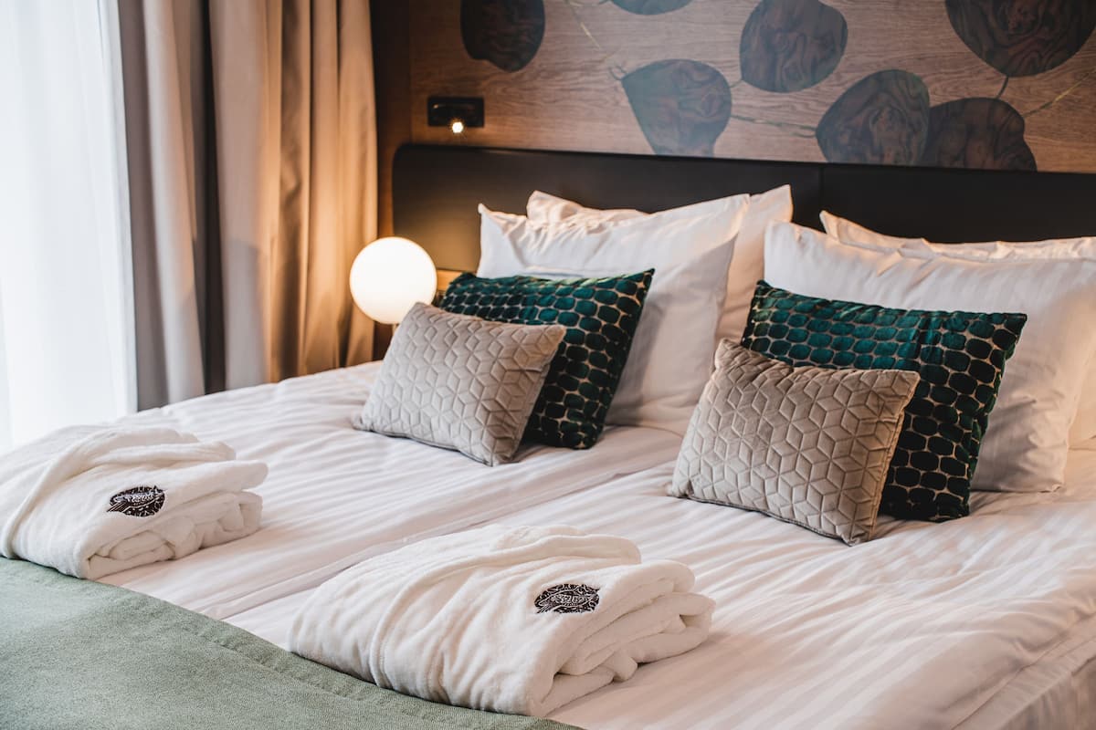 A neatly made bed with white linens and decorative pillows, a green throw blanket, and a wall with a wooden pattern.