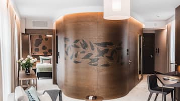 Une chambre d’hôtel moderne avec un grand mur décoratif en bois, un coin repas avec une table et des chaises, un canapé avec des coussins et une petite table d’appoint agrémentée d’un vase de fleurs.
