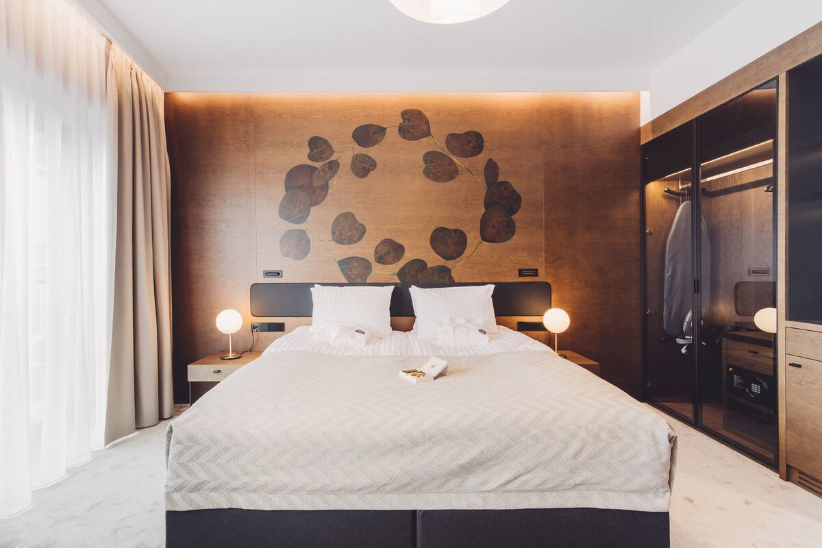 A modern hotel room with a large bed, wooden headboard, and a unique wall art piece.
