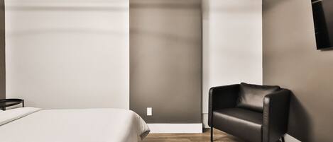 A modern bedroom with a bed, a black leather chair, and a wooden floor.