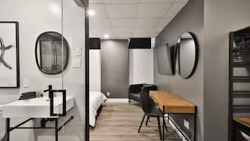 Une chambre d’hôtel moderne équipée d’un lit, d’un bureau, d’une chaise, d’un miroir rond et d’une armoire.