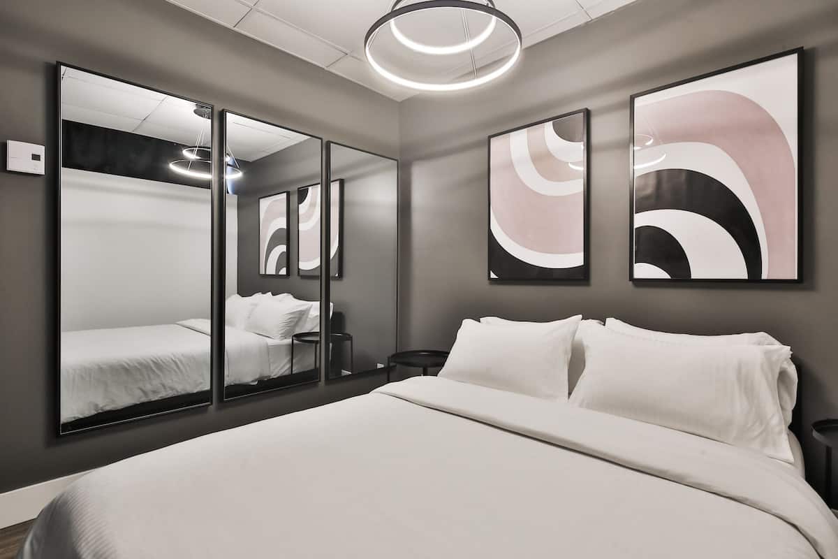 Une chambre d’hôtel moderne avec un grand lit, une table de chevet, un miroir, des œuvres d’art abstraites accrochées au mur et un luminaire au plafond.