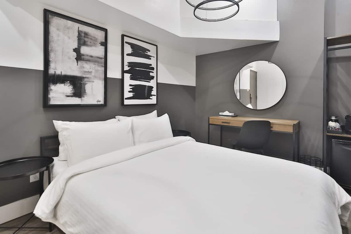 Une chambre d’hôtel moderne, équipée d’un lit, d’un bureau et d’un miroir rond.