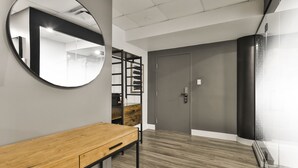 Un espace de bureau moderne comprenant un bureau en bois, un miroir rond, une étagère et une porte dotée d’un système de verrouillage à clavier.