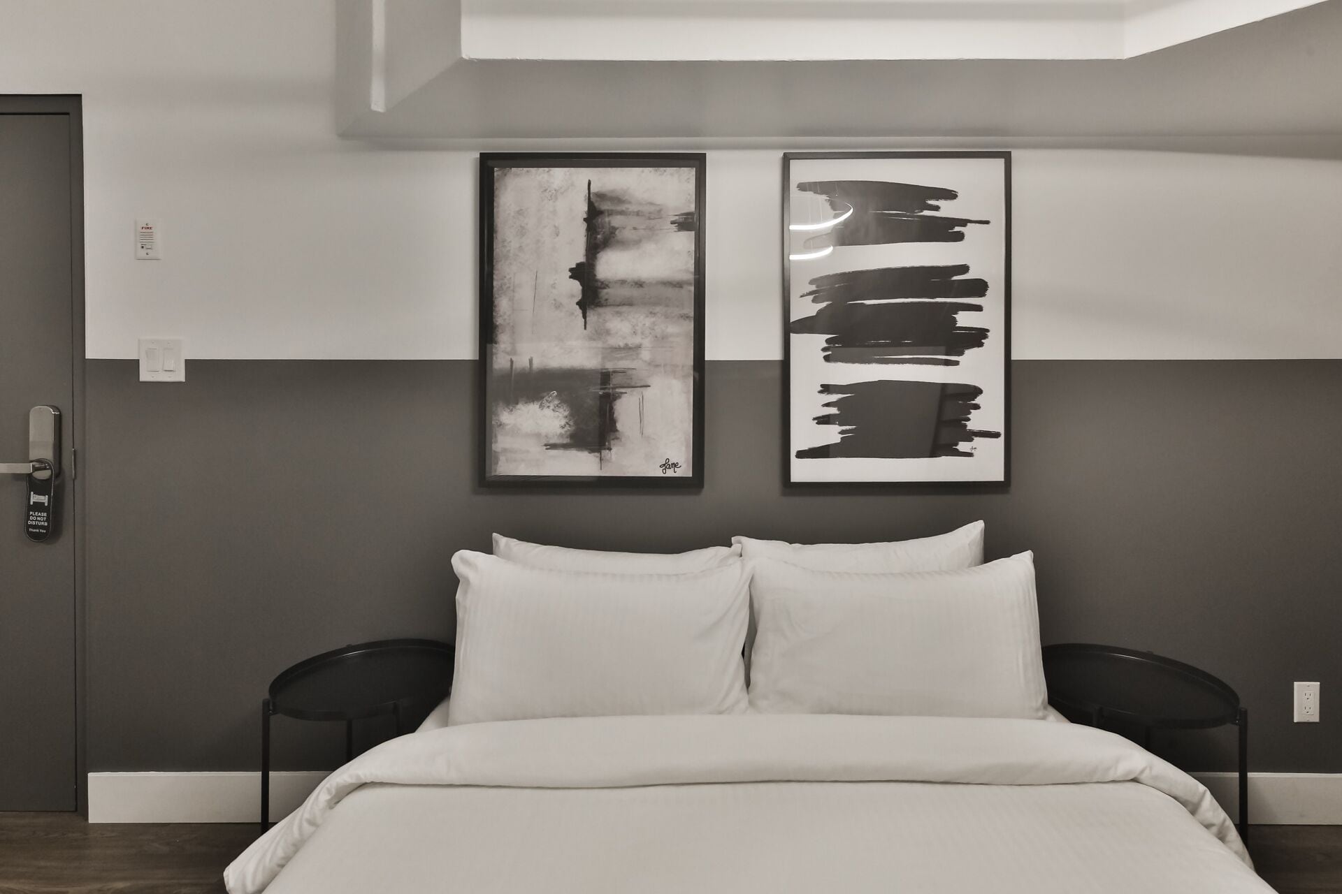 Ein modernes Schlafzimmer mit einem Bett, zwei schwarzen Sesseln und zwei abstrakten Bildern an der Wand.