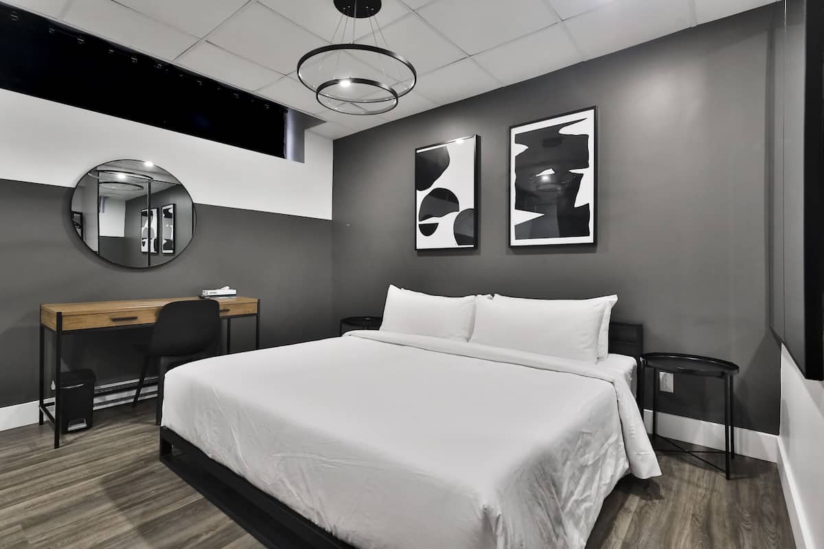 Une chambre d’hôtel moderne avec un grand lit, un bureau, une chaise, un miroir rond et deux tableaux abstraits accrochés au mur.