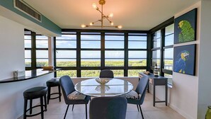 A dining area with a round table, chairs, and a view of the landscape through large windows. - South Seas Tower 4- 812: Beautifully Updated; Large Balcony (Marco Island)