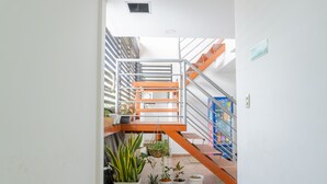 A staircase with metal railings and orange accents, leading to an upper level. There are potted plants on the lower landing.