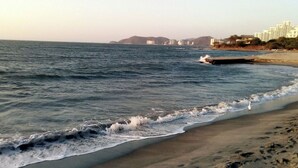 A beach with waves, a sandy shore, and buildings in the background.