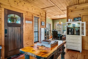 Un intérieur rustique en bois, avec une porte en bois, un coin repas comprenant une table et des chaises, et une petite cuisine équipée d’une machine à café.