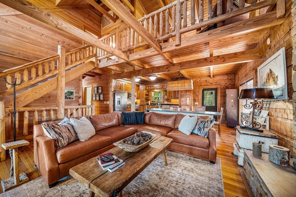 L'intérieur d'une cabane en rondins, avec un grand escalier en bois, un canapé d'angle en cuir, une table basse en bois et une décoration rustique.