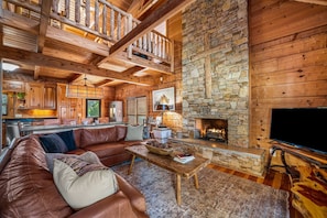 L’intérieur d’un chalet confortable, avec une cheminée en pierre, un canapé en cuir et un téléviseur.