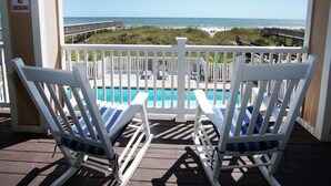 A balcony with two white rocking chairs facing a pool and ocean view. - Condo w/ocean & salt marsh view balcony, steps to the beach w/fitness center, indoor & outdoor pools (North Myrtle Beach)
