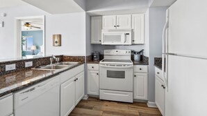 A compact kitchen with white cabinetry, a granite countertop, a built-in microwave, and a stainless steel sink. - Condo w/ocean & salt marsh view balcony, steps to the beach w/fitness center, indoor & outdoor pools (North Myrtle Beach)