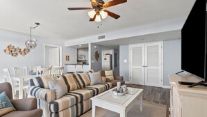 A modern living room with a striped sofa, a white coffee table, and a ceiling fan. - Condo w/ocean & salt marsh view balcony, steps to the beach w/fitness center, indoor & outdoor pools (North Myrtle Beach)