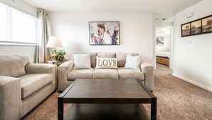 A living room with a beige sofa, a matching armchair, a coffee table, and a painting of horses. - ◆ Sensational Apartment! 2 Bed 1 Bath - Sleeps 4 ◆ (Colorado Springs)