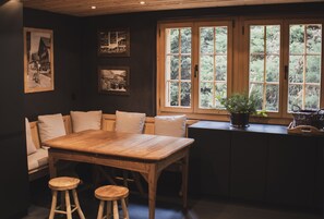 Ein Holztisch mit vier Stühlen, eine Bank mit Kissen und ein Fenster mit Blick ins Grüne.