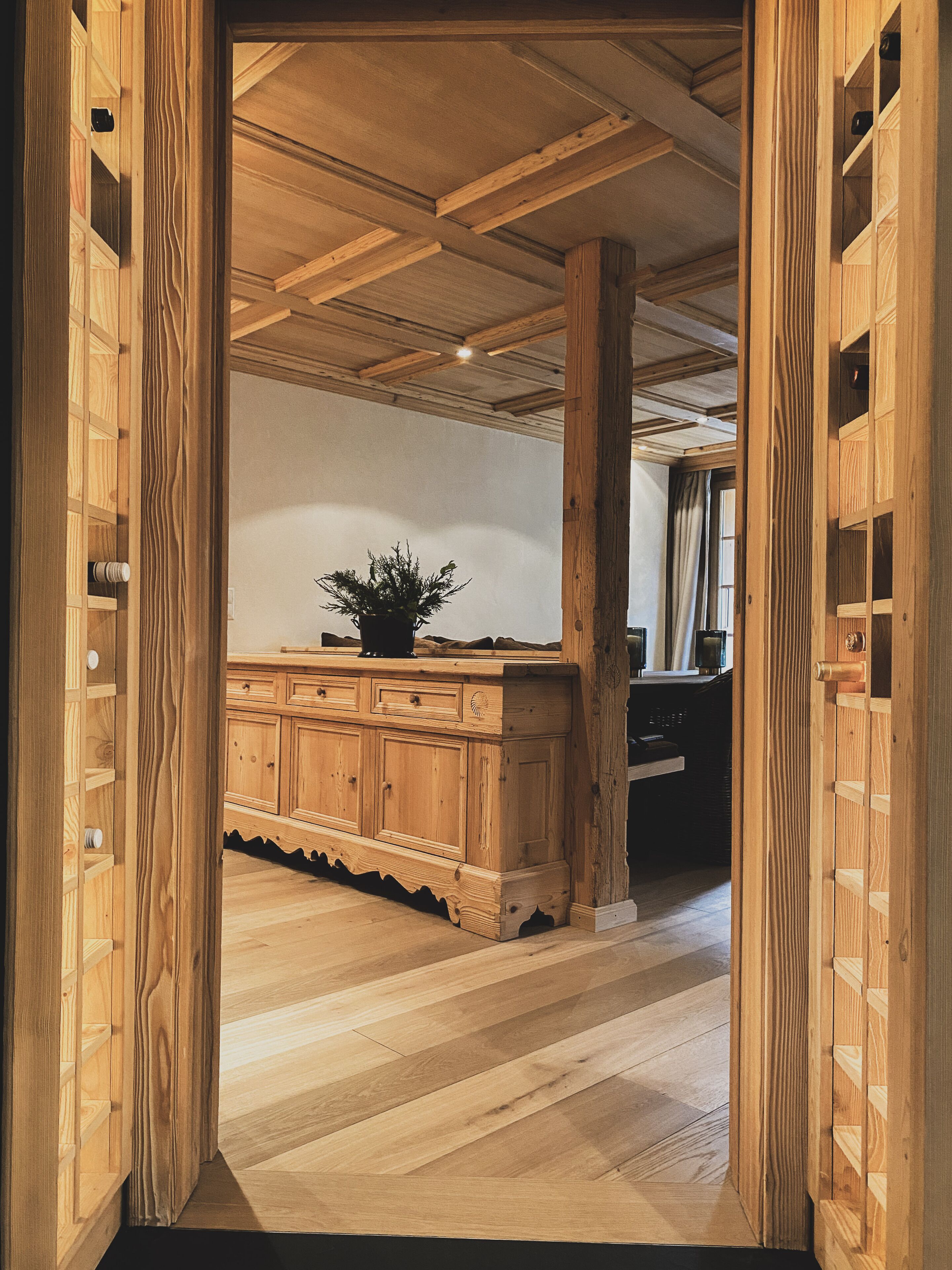 Un intérieur en bois avec un îlot central, des poutres en bois au plafond et une plante en pot sur l’îlot.