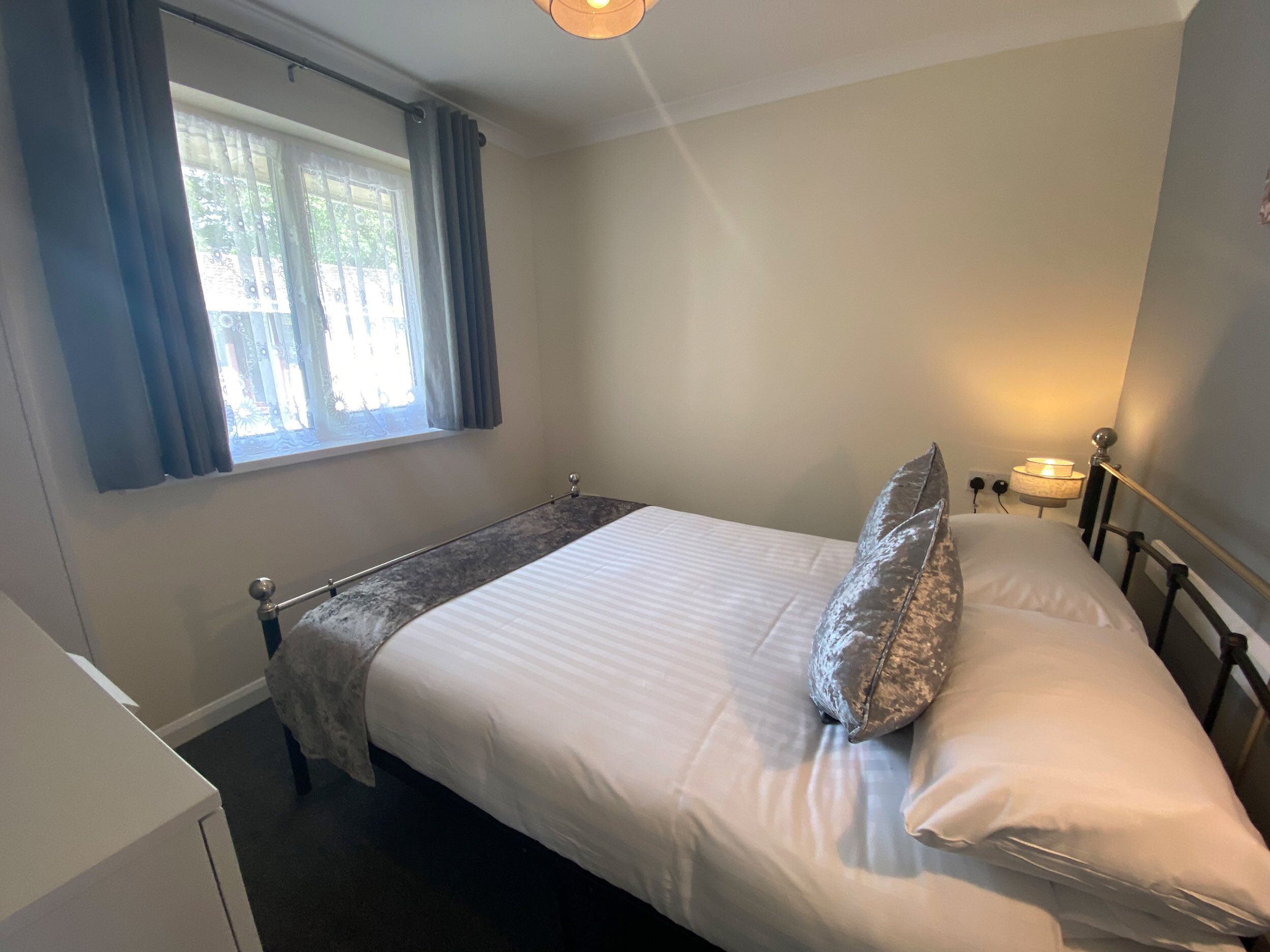 Een enkel bed met hoofdeinde, een nachtkastje met lamp en een raam met gordijnen.