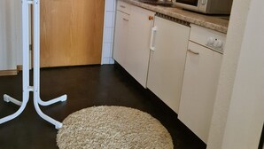 A small kitchen with a microwave, a coffee maker, and a telephone on the counter. There is a wooden door and a white cabinet. A beige rug is on the floor. - Apartment  (Basilea)