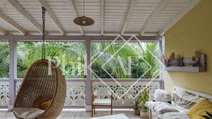 A room with a hanging chair, a sofa, a table with decorative items, and a view of lush greenery outside.