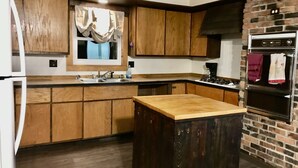Una cocina con armarios de madera, una isla central, horno empotrado y una ventana con cortinas.