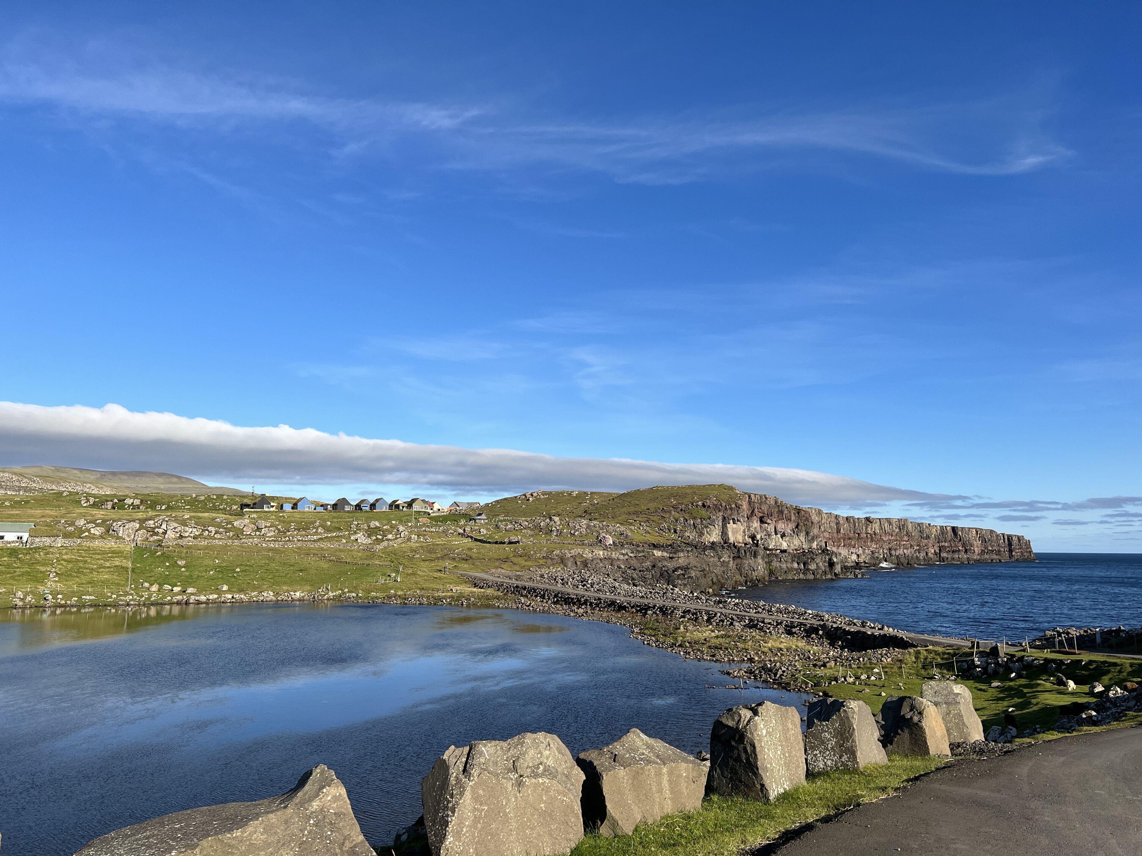 A coastal landscape with a clear sky, rocky cliffs, and a calm body of water.