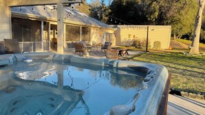 Un bain à remous entouré de pierres, un patio couvert avec des meubles d’extérieur, et une maison dotée d’un porche abrité.