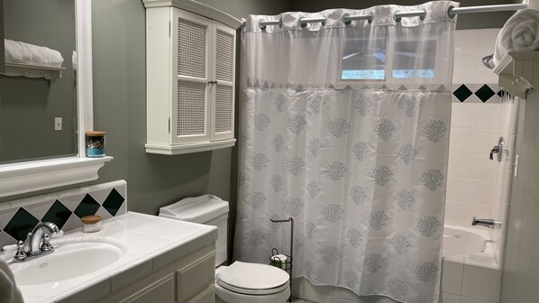 A bathroom with a white sink, toilet, and bathtub. There is a window above the sink and a shower curtain with a leaf pattern.