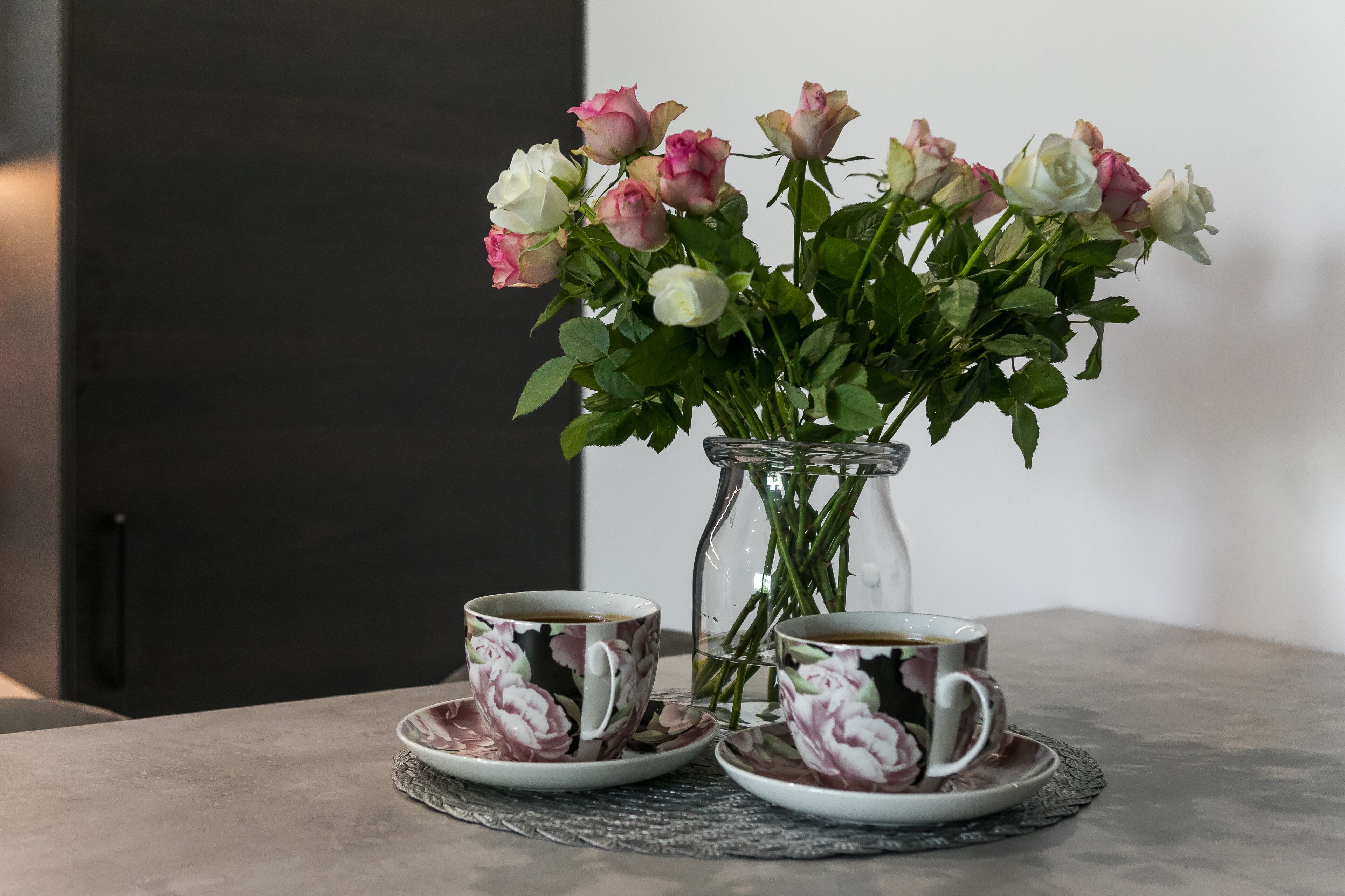 A vase with roses and two cups on a table.