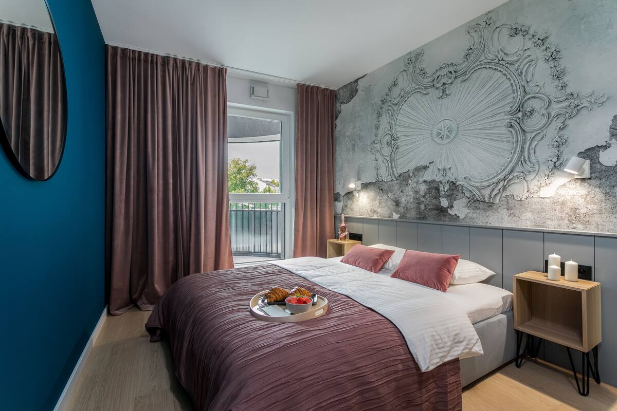 A modern bedroom with a large bed, a side table with candles, and a decorative wall mural.