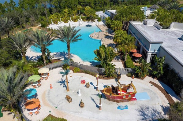 Relax by the resort's large pool surrounded by lounge chairs and umbrellas, with a boat-shaped water feature in the center.