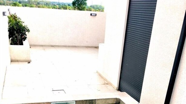 Une piscine à l’eau claire, entourée d’une terrasse carrelée et d’un mur blanc agrémenté d’un volet noir.