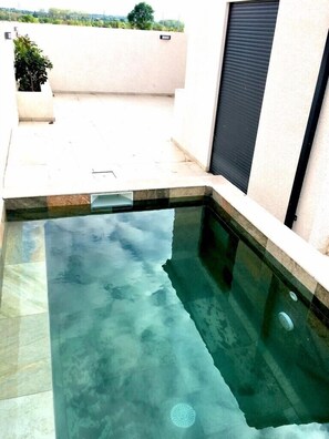 A swimming pool with clear water, surrounded by a tiled deck and a white wall with a black shutter. - The 4-star MAISON de Laurie with pool (Pézenas)