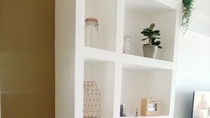 Une étagère blanche, ornée de divers objets décoratifs, sur laquelle se trouve une plante en pot et un téléviseur.