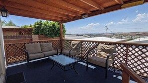 A covered outdoor seating area with a table and chairs, a wooden fence, and a view of the surrounding landscape. - Parker, AZ - Hilltop Hideaway (Parker)