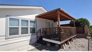 A house with a covered porch, a small outdoor seating area, and a gravel driveway. - Parker, AZ - Hilltop Hideaway (Parker)