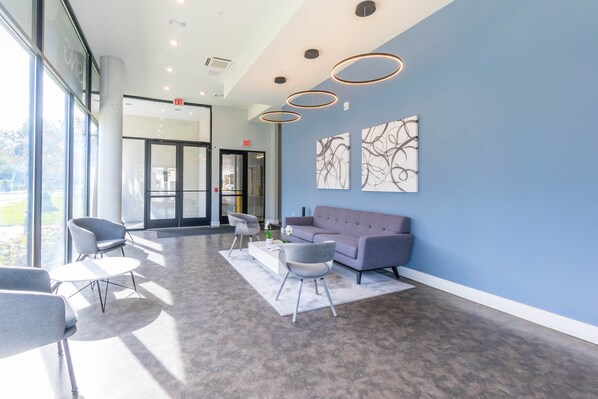 A modern lobby with a grey sofa, two grey armchairs, a white coffee table, and abstract wall art.