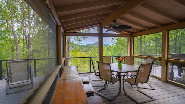 Un espace extérieur abrité, avec une table et des chaises, offrant une vue sur un paysage boisé.