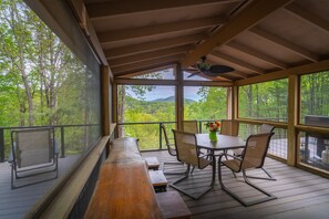 A covered outdoor seating area with a table and chairs, overlooking a forested landscape. - Hide Away, Peaceful, Cozy cabin  (Cleveland)