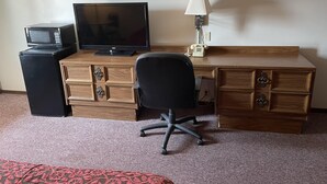 A hotel room with a wooden desk, a black office chair, a television, a microwave, and a telephone.