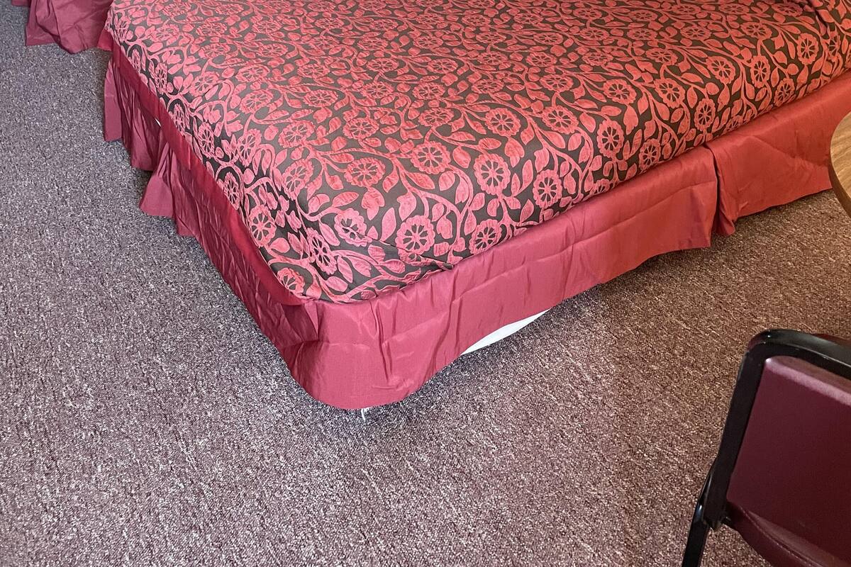 A hotel room with two beds, a nightstand, a lamp, and a chair.