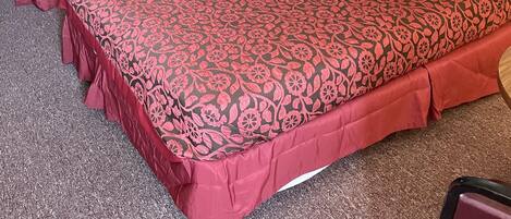 A hotel room with two beds, a nightstand, a lamp, and a chair.