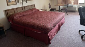 A hotel room with a large bed, a desk, a chair, a lamp, and a window with curtains.