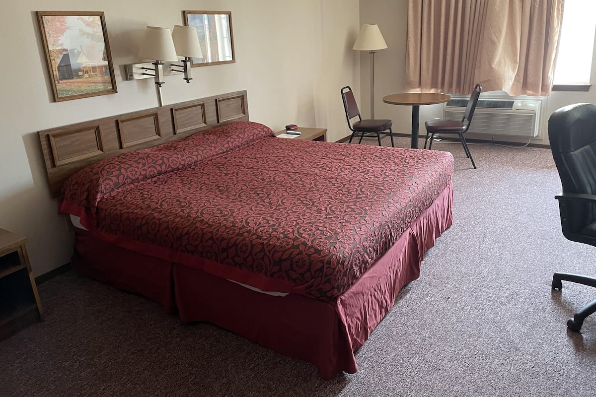 A hotel room with a large bed, a desk, a chair, a lamp, and a window with curtains.