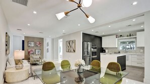 A modern kitchen with stainless steel appliances, a dining area with a glass table and green chairs, and a living area with a sofa and lamp. - Renovated 4 Bedroom home, tastefully designed! (Miami)