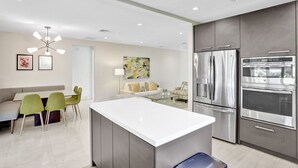 A modern kitchen with stainless steel appliances, a central island, and a dining area with green chairs. - Renovated 4 Bedroom home, tastefully designed! (Miami)