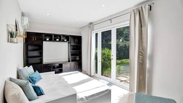 Ein Schlafzimmer mit einem großen Bett, eingebauten Regalen, einem Fenster mit Vorhängen und Blick ins Grüne.