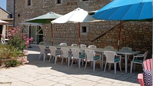 Ein Steinhaus mit Terrasse, Sitzgelegenheiten und Sonnenschirmen.
