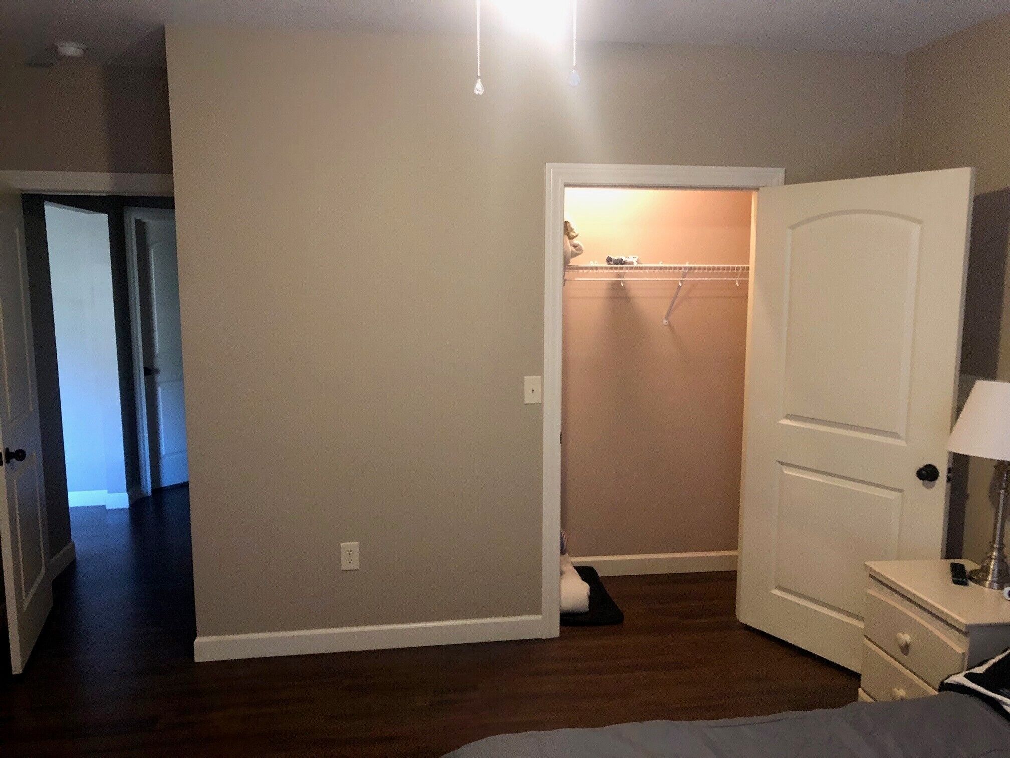 Een slaapkamer met een bed, nachtkastje, lamp, kast en een deur naar een andere kamer.